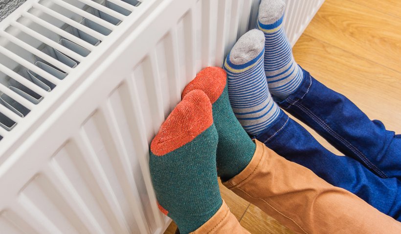 Woman and child wearing colorful pair of woolly socks warming cold feet in front of heating radiator in winter time. Electric or gas heater at home.