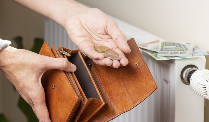 Woman's hand takes euro money from wallet and places on heating radiator battery with temperature regulator. Expensive heating costs during cold season. Paying bills